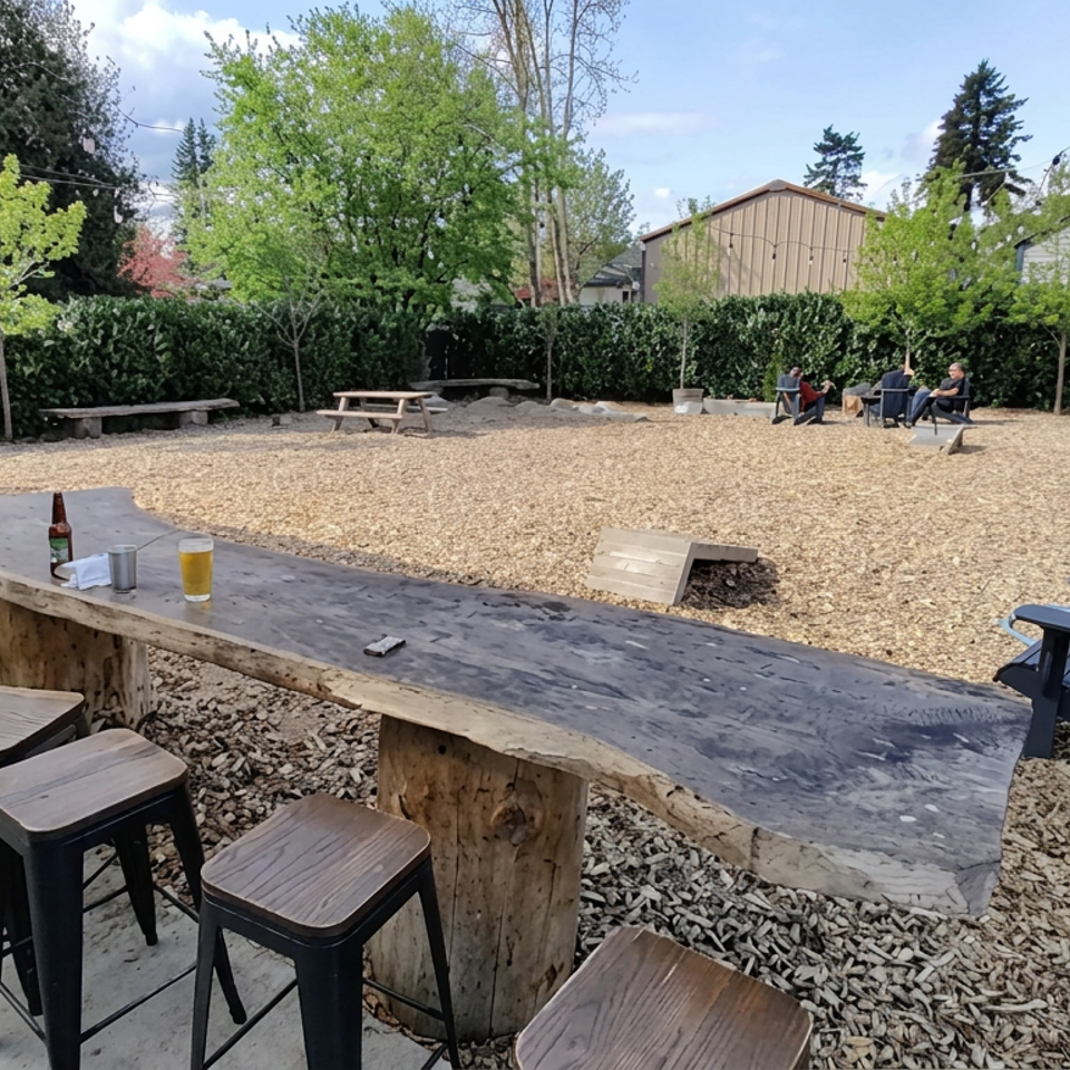 Outdoor restaurant beer garden with rustic wooden bar, stools, picnic tables, lounge chairs, string lights, and a gravel lawn.